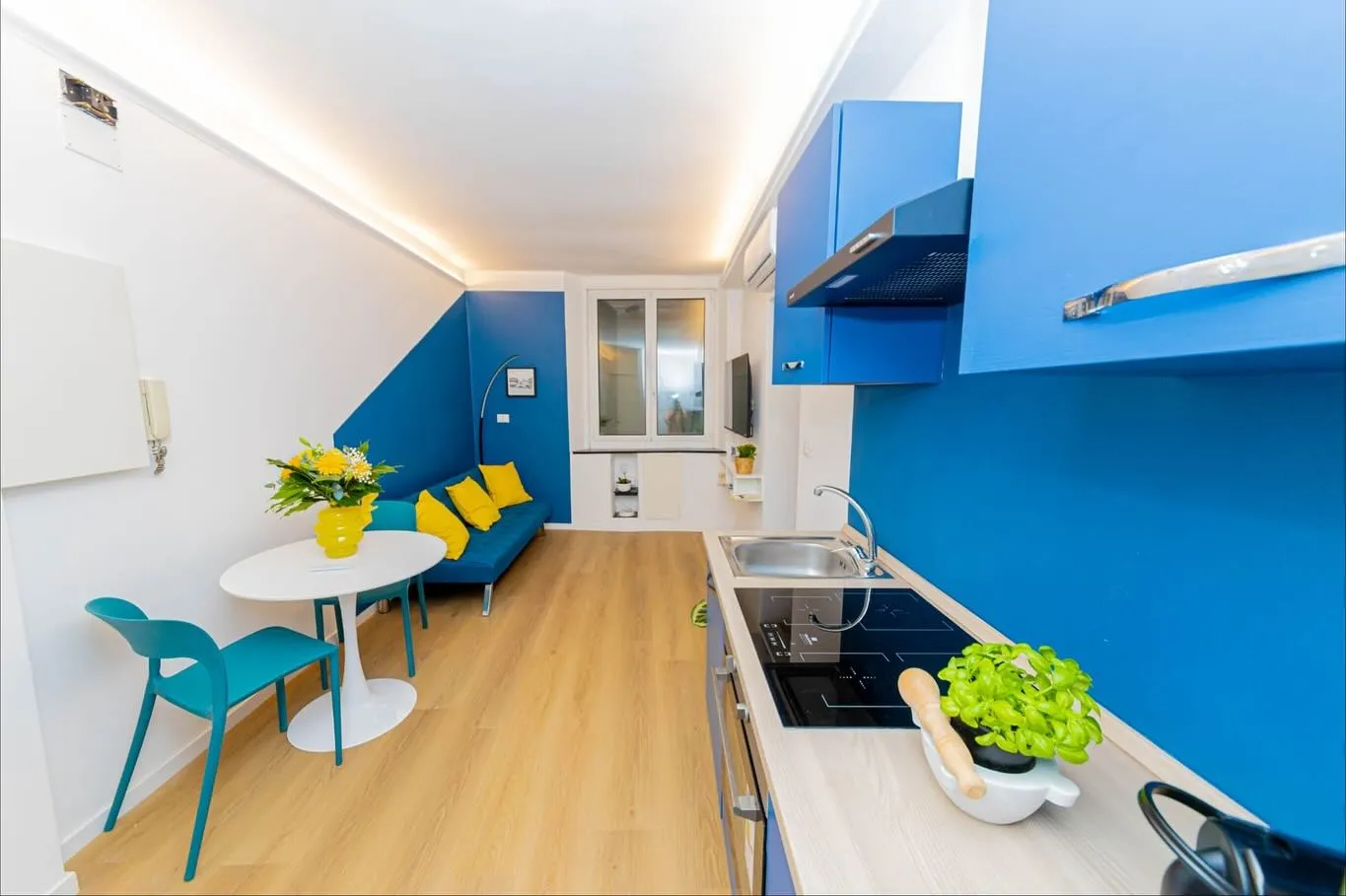 Cucina open space con parete blu, pensili bianchi e tavolino con sedie azzurre