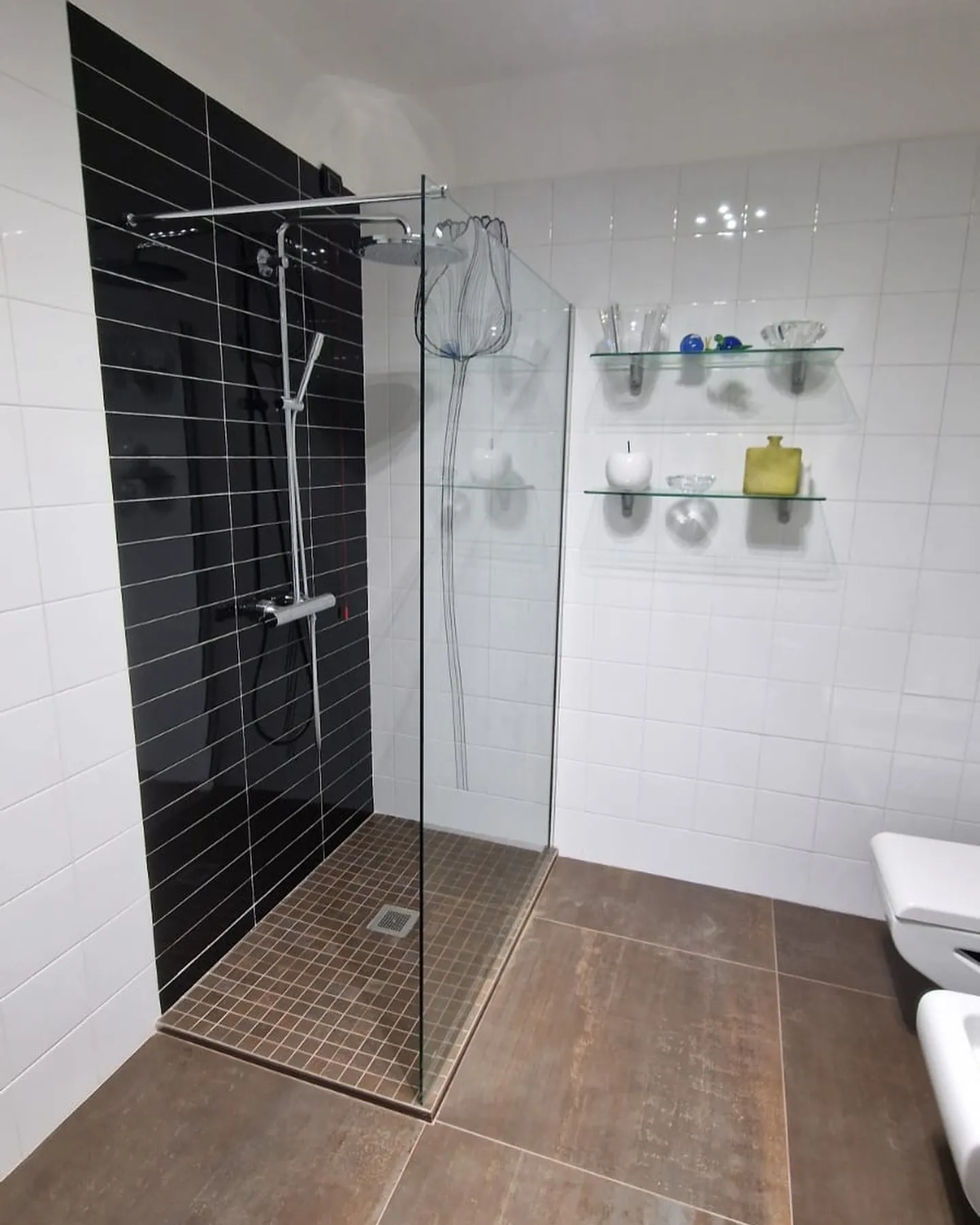 Bagno con doccia walk-in, parete di piastrelle nere e pavimento effetto legno