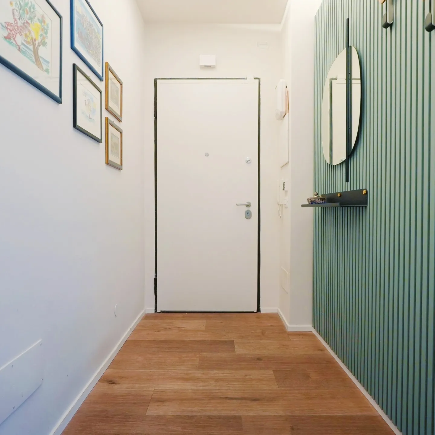 Ingresso ristrutturato con boiserie a doghe verde salvia, specchio tondo e pavimento in legno