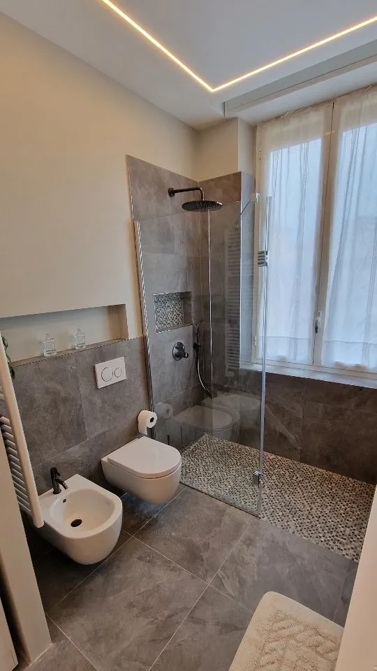 Bagno con rivestimenti grigi, doccia con nicchia e luce LED nel controsoffitto