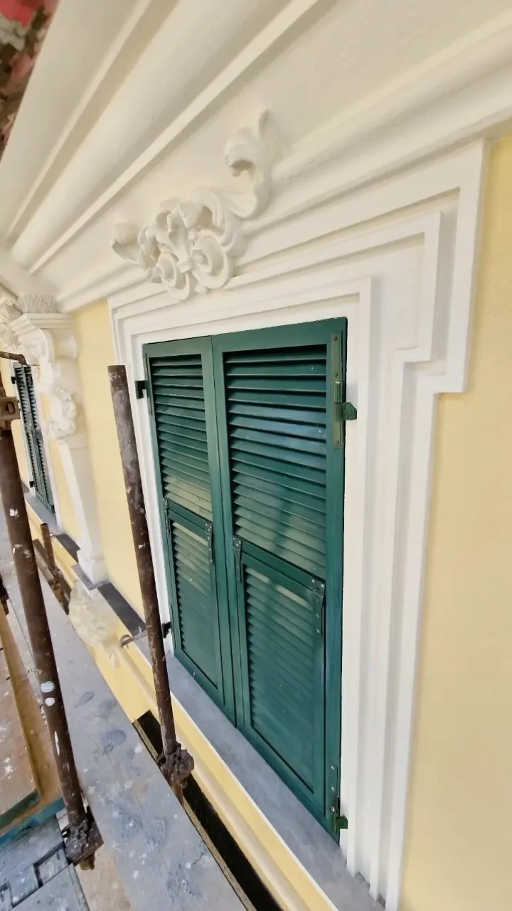 Finestra con persiane verdi e cornice decorata restaurata su facciata gialla