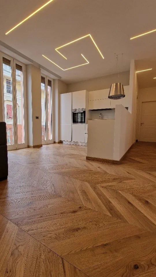 Open space con parquet a spina di pesce, luci LED lineari nel soffitto e cucina bianca