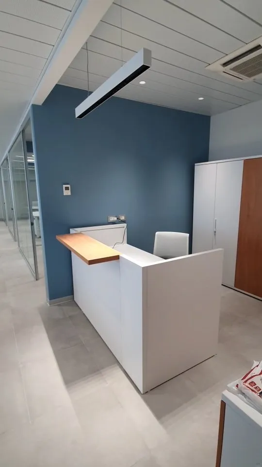 Reception di uffici con bancone bianco, parete blu e controsoffitto
