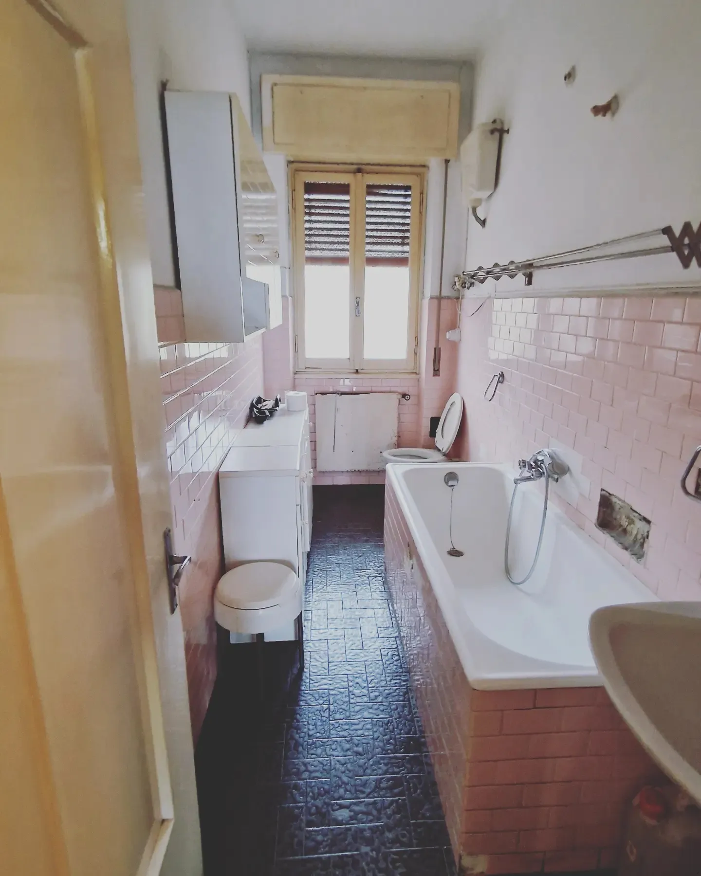 Bagno prima della ristrutturazione: piastrelle rosa, vasca e pavimento scuro