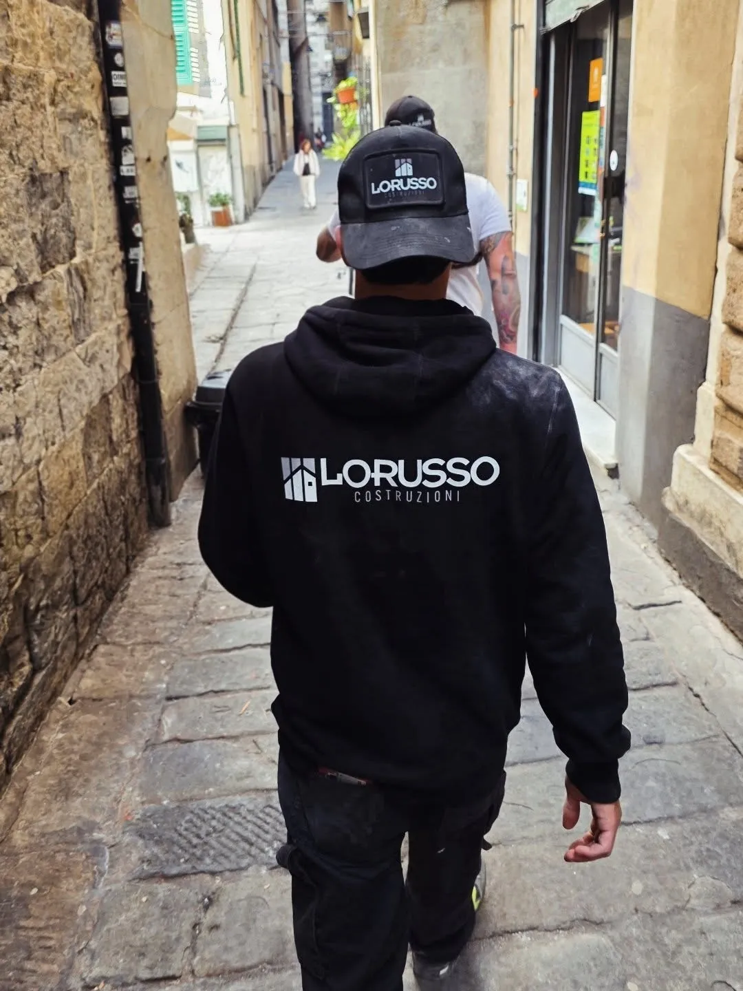 Operaio di Lorusso Costruzioni con la felpa dell'impresa cammina in un caruggio del centro storico di Genova